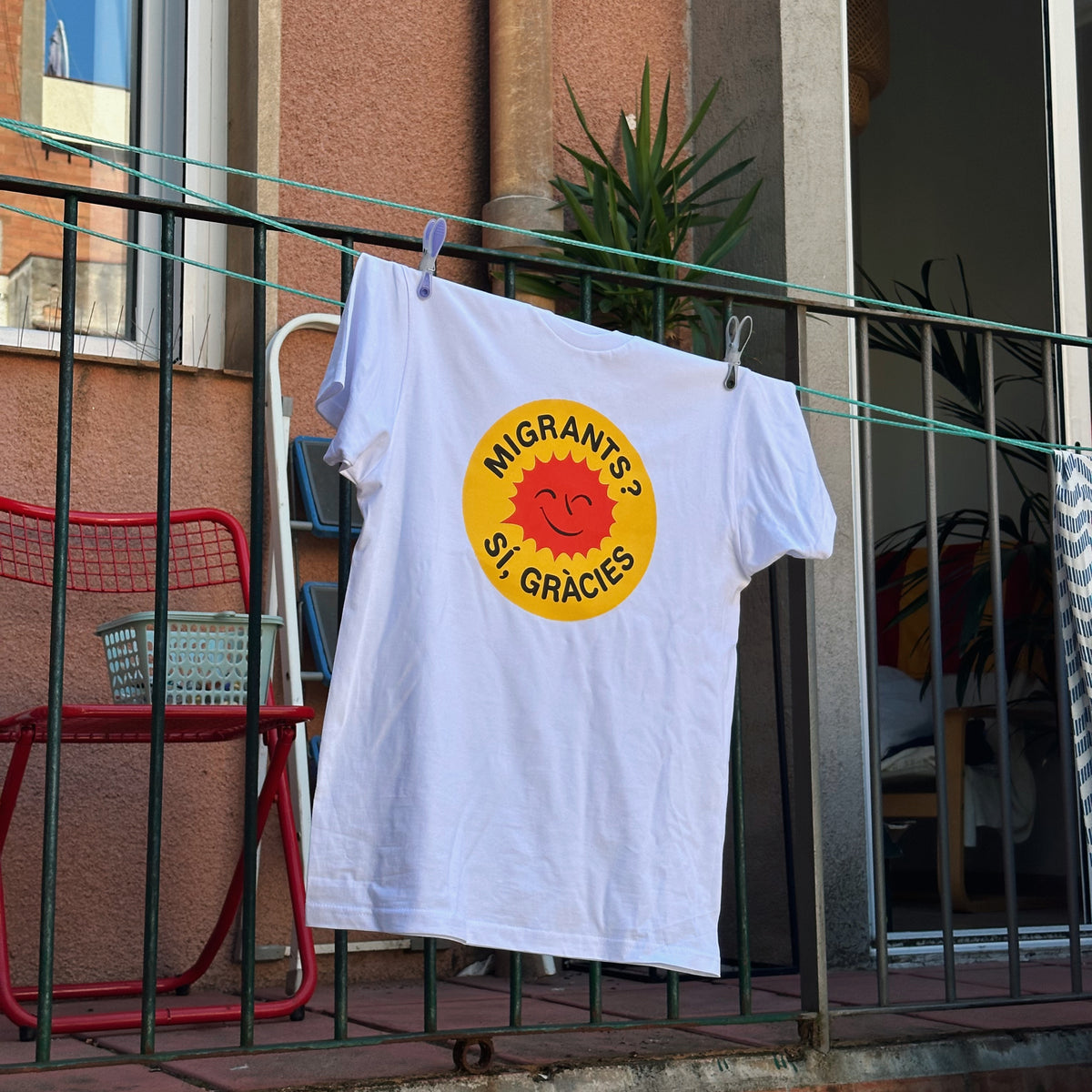Samarreta blanca «Migrants? Sí, gràcies» de L'altra ciutat estesa en un balcó